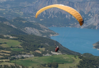 Parapendio che sorvola campi verdi e un lago blu vicino a Le Vernet in Provenza-Alpi-Costa Azzurra, Francia.