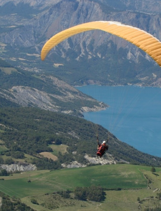 Parapendio che sorvola campi verdi e un lago blu vicino a Le Vernet in Provenza-Alpi-Costa Azzurra, Francia.