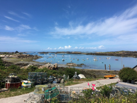 Vista de botes y trampas de pesca en Camping O2 en Normandía, Francia, con cielo azul y costa rocosa.