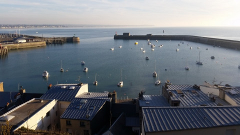 Vista de un puerto con barcos desde Camping O2, un parque vacacional en Normandía, Francia, con tejados delante.