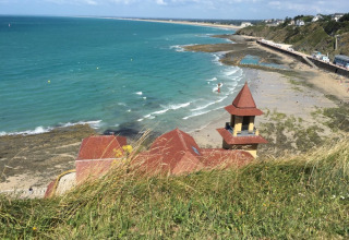 Vista sulla spiaggia e sul mare blu vicino a Longueville, Normandia, Francia, con edificio costiero in primo piano.