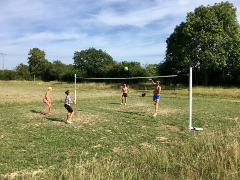 Vier mensen spelen volleybal in de buitenlucht op het gras van Camping O2 vakantiepark in Normandië, Frankrijk.