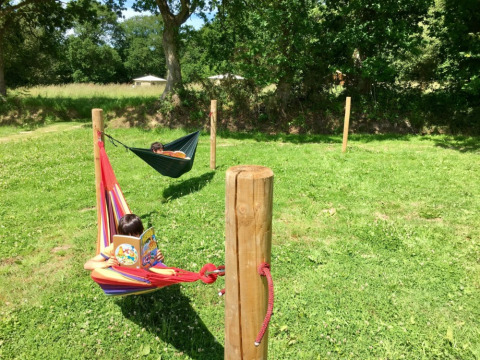 Dos niños leen libros en coloridas hamacas sobre césped en Camping O2, un parque vacacional en Normandía, Francia.