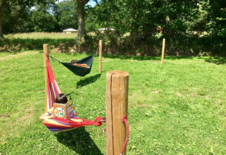 Two children read books in colorful hammocks on grass at Camping O2, a holiday park in Normandy, France.
