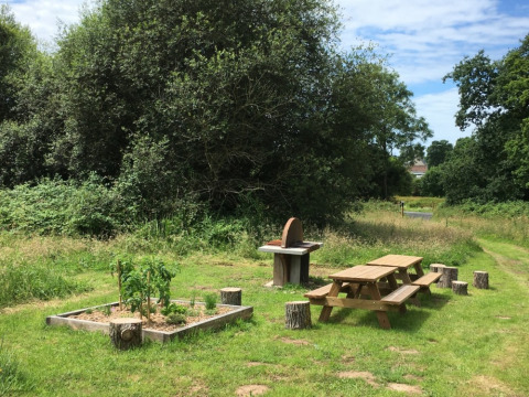 Udendørs picnicområde med træborde, grill og en lille køkkenhave ved Camping O2 i Normandiet, Frankrig.