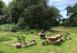 Udendørs picnicområde med træborde, grill og en lille køkkenhave ved Camping O2 i Normandiet, Frankrig.