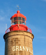 Lystårn ved Granville tæt på Longueville i Normandiet, Frankrig, med rød top og blå himmel baggrund.