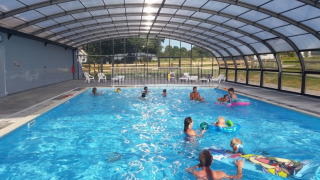 Overdækket swimmingpool med familier, der svømmer og leger, på Camping O2 feriepark i Normandiet, Frankrig.