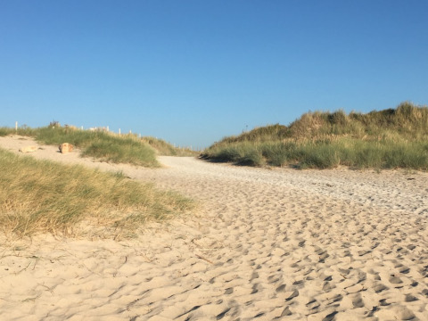 Zandpad tussen grasduinen en blauwe lucht bij Camping O2 vakantiepark in Normandië, Frankrijk.