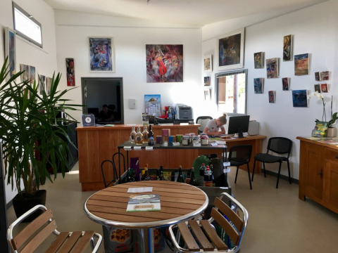 Recepción de Camping O2 en Normandía, Francia, con arte en las paredes, mesa y personal trabajando.