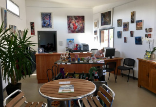 Receptionen på Camping O2 i Normandiet, Frankrig, med borde, stole, kunst på væggen og personale.