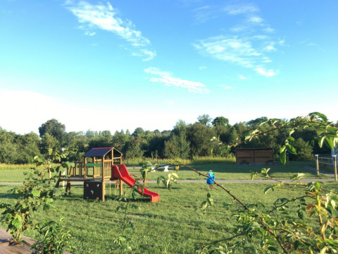 Speeltuin bij Camping O2, vakantiepark in Normandië, Frankrijk, met rode glijbaan en groene weide.