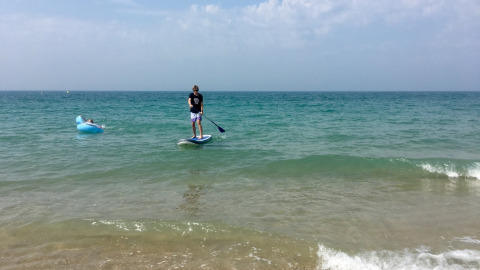 Een persoon op een paddleboard en een ander op een opblaasmatras in zee bij een strand in Normandië, Frankrijk.