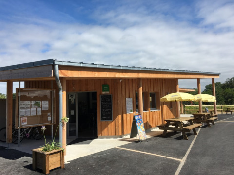 Wooden building with outdoor seating and umbrellas at Camping O2, a holiday park in Normandy, France.