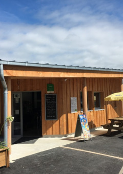 Træbygning med udendørs siddepladser og parasoller i Camping O2, en feriepark i Normandiet, Frankrig.