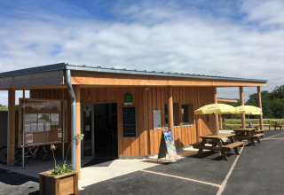 Træbygning med udendørs siddepladser og parasoller i Camping O2, en feriepark i Normandiet, Frankrig.