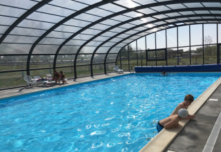 Covered swimming pool at Camping O2 in Normandy, France, with children swimming and adults relaxing by the pool.