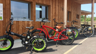 Udlejning af farverige elektriske cykler foran en træbygning på Camping O2 feriepark i Normandiet, Frankrig.