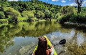 Donna in kayak pagaia su un fiume limpido circondato da foreste a Camping du Rivage, Diekirch, Lussemburgo.