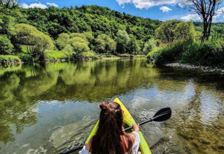 Vrouw kajakt op een heldere rivier omgeven door bos bij Camping du Rivage, Diekirch, Luxemburg.