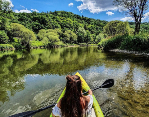 Woman kayaking on a clear river surrounded by lush forest at Camping du Rivage, Diekirch, Luxembourg.