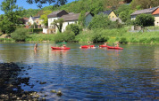 Kinder paddeln in roten Kanus auf einem Fluss bei Camping du Rivage, umgeben von Häusern in Diekirch.