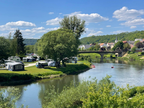 Campamento junto al río en Camping du Rivage, Diekirch, Luxemburgo, con casas rodantes y kayaks bajo el sol.