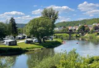 Kampeerplaats aan de rivier bij Camping du Rivage in Diekirch, Luxemburg, met caravans en kano’s op een zonnige dag.
