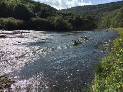 Mensen kajakken op een rivier omgeven door groene heuvels bij Camping du Rivage in Diekirch, Luxemburg.
