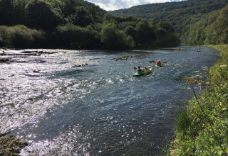 Des personnes font du kayak sur une rivière entourée de collines vertes au Camping du Rivage à Diekirch.