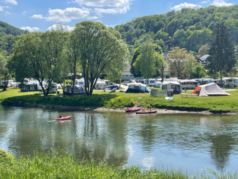Campeggio sul fiume a Diekirch, Lussemburgo, con tende, roulotte e canoe tra colline e alberi verdi.
