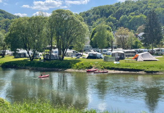 Riverside campsite in Diekirch, Luxembourg with tents, caravans and canoes, set among green hills and trees.