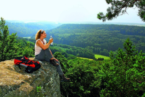 Woman enjoys scenic forest view from a rock at Camping du Rivage holiday park, Diekirch, Luxembourg.