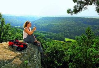 Woman enjoys scenic forest view from a rock at Camping du Rivage holiday park, Diekirch, Luxembourg.