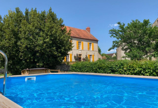 Blauw zwembad voor een geel huis met oranje luiken in Auvergne-Rhône-Alpes, Frankrijk, bij zonnig weer.