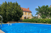 Pool mit klarem Wasser vor einem gelben Haus mit orangefarbenen Fensterläden in Auvergne-Rhône-Alpes, Frankreich.