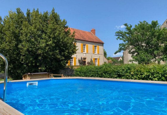Pool mit klarem Wasser vor einem gelben Haus mit orangefarbenen Fensterläden in Auvergne-Rhône-Alpes, Frankreich.