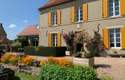 Charmerende feriepark Minicamping Sous les Cloches i Auvergne-Rhône-Alpes med farverige blomster og gulmalede skodder.