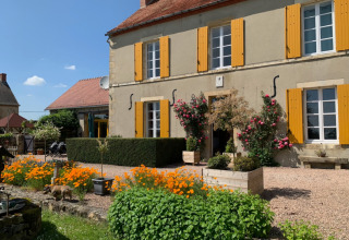 Charmerende feriepark Minicamping Sous les Cloches i Auvergne-Rhône-Alpes med farverige blomster og gulmalede skodder.