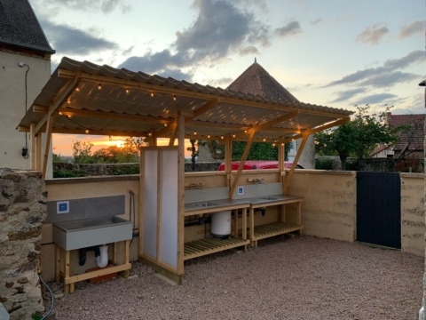 Estación de lavado de platos al aire libre con techo y luces al atardecer en Minicamping Sous les Cloches, Francia.