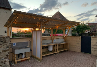 Estación de lavado de platos al aire libre con techo y luces al atardecer en Minicamping Sous les Cloches, Francia.