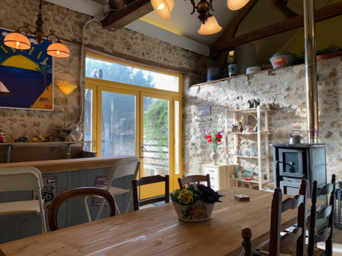 Intérieur chaleureux avec murs en pierre, table en bois et poêle au Minicamping Sous les Cloches, France.