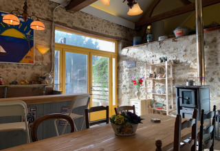 Intérieur chaleureux avec murs en pierre, table en bois et poêle au Minicamping Sous les Cloches, France.