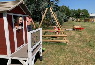 Niños juegan fuera en una casita, columpios y arenero en un parque de vacaciones en Francia.