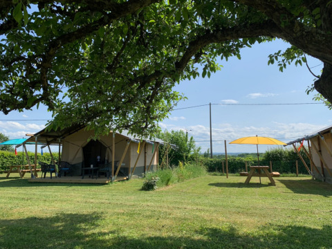 Blick auf Zelte, Picknicktische und Sonnenschirme im Minicamping Sous les Cloches in Auvergne-Rhône-Alpes, Frankreich.