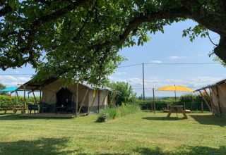 Zicht op tenten, picknicktafels en parasols bij Minicamping Sous les Cloches in Auvergne-Rhône-Alpes, Frankrijk.