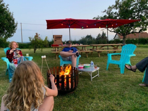 Menschen sitzen um ein Lagerfeuer und rösten Marshmallows im Minicamping Sous les Cloches, Frankreich.