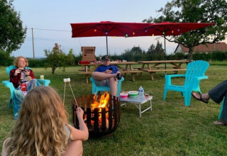 Menschen sitzen um ein Lagerfeuer und rösten Marshmallows im Minicamping Sous les Cloches, Frankreich.