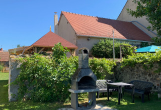 Zona de jardín al aire libre con barbacoa, mesas y sillas en Minicamping Sous les Cloches en Auvergne-Rhône-Alpes, Francia.