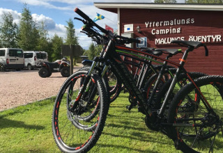 Cykler parkeret på græs ved Yttermalungs Camping i Dalarna, Sverige, med skilte og bygning i baggrunden.